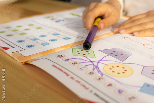 Child's hands doing the task in the book. Little child doing counting tasks, indoors. Elementary school and education: preschool education, child development concept.