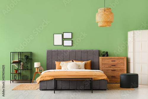 Comfortable bed, pillows and wooden chest of drawers in stylish bedroom
