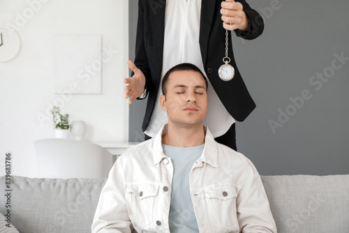 Female psychologist with pocket watch hypnotizing young man in office