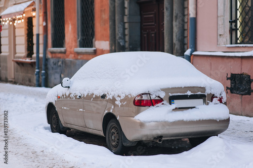 A passenger car is covered with snow and stands on a narrow street in the center of Lviv, Ukraine. Concept of severe winter weather in Europe.