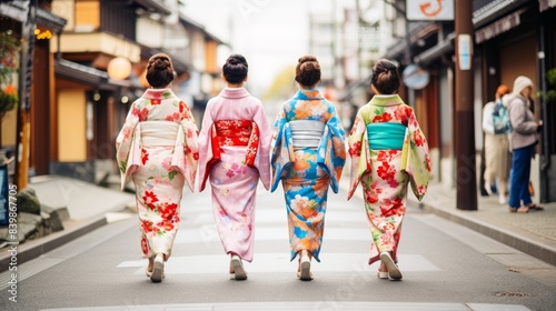 Women in traditional Japanese kimonos walk down a street. The women are wearing different colored kimonos, and they are walking in a line