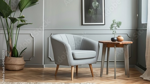 Grey armchair with plant and poster in the interior living room, next to wooden table