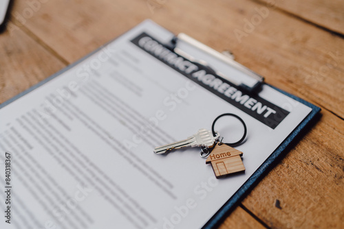 Close-up of a tenancy agreement document with a small house keychain on a wooden table, symbolizing real estate or rental property contract.