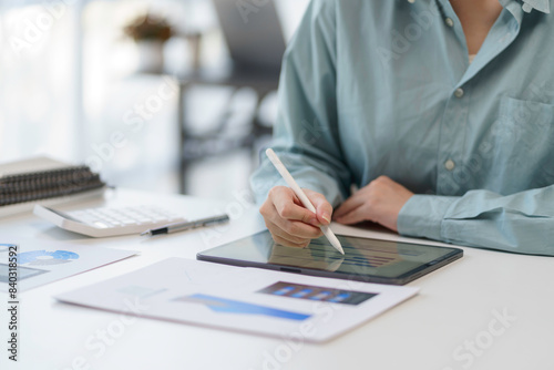 Person using a tablet with a stylus in a modern office environment, working on digital documents and data charts.