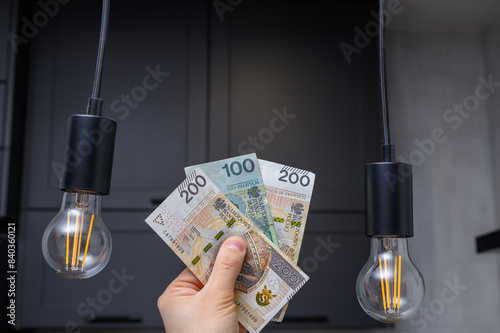 Rachunek za prąd energię elektryczną, polskie pieniądze pln w dłoniach obok żarówek 