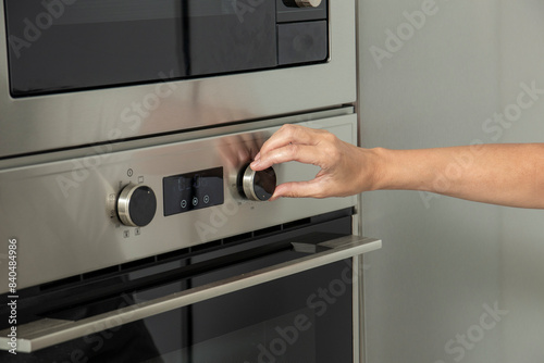 A hand adjusts a knob on a modern stainless steel oven, likely setting the temperature or cooking mode