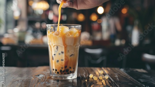 A hand stirring a glass of brown sugar bubble milk tea, the rich caramel hue swirling with the creamy base, promising a decadent treat for the taste buds