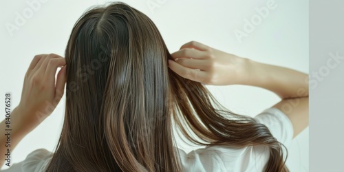 A woman with long brown hair is straightening her locks in front of a mirror