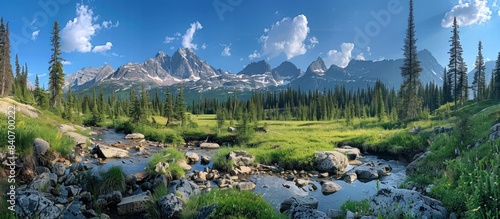 panoramic photo of the rocky mountains, steep mountain range with snowcapped peaks stands against a blue sky.