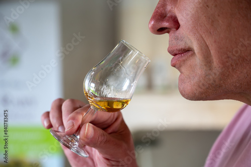 Enologist tastis and sniffs cognac spirit aged in old dark French oak barrels in cellar distillery house, Cognac white wine region, Charente, Segonzac, Grand Champagne, France