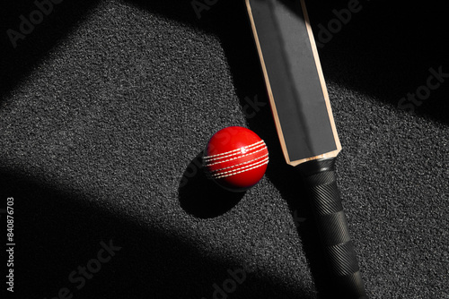 Cricket bat and red ball with natural lighting on black background. Horizontal sport theme poster, greeting cards, headers, website and app