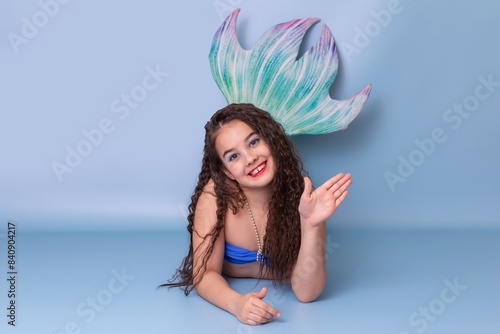 Beautiful smiling girl in a mermaid costume, friendly, lies on a blue background . Copy space