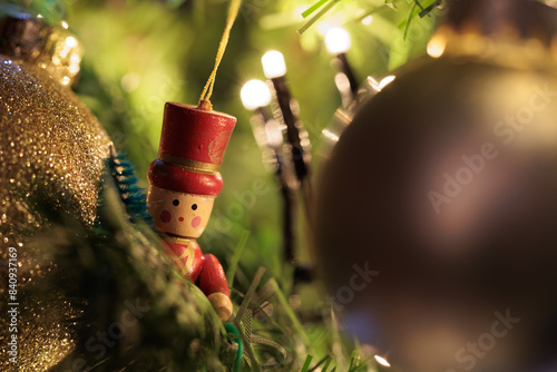 piccolo omino di legno appeso ad un albero di natale, circondato da luci ed altre decorazioni in tema natalizio