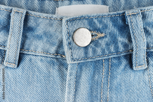 Front side of blue jeans pants with metal button closeup, macro. Denim background, texture, wallpaper, fashion concept. Design detail and seams.