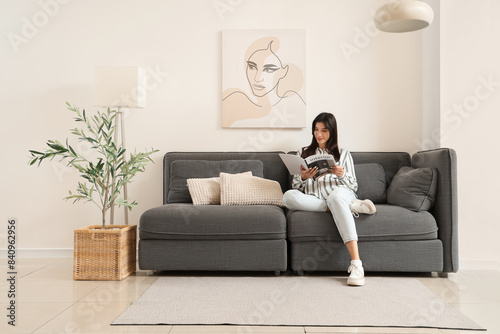 Young woman reading magazine on black sofa in living room