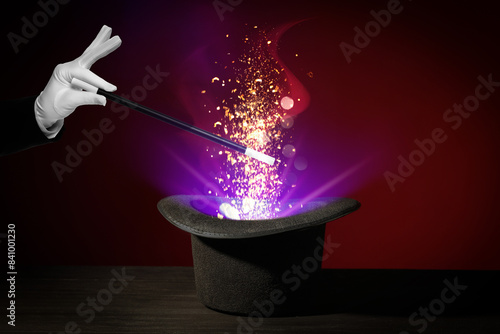 Wizard conjuring magical light out of hat with wand on dark background, closeup