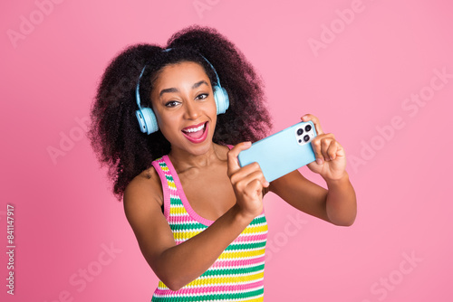 Photo of nice woman with perming coiffure dressed knitwear tank in headphones take shoots on smartphone isolated on pink color background
