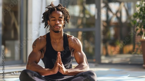 A young man with dreadlocks sits cross-legged on a patio, eyes closed, meditating with his hands in prayer position.