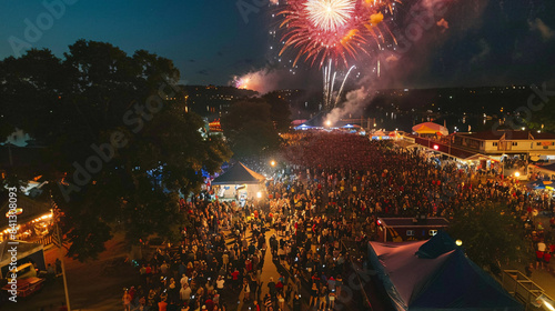 An aerial view of a large crowd gathered for an Independence Day event, with colorful decorations and fireworks overhead