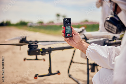 A male operator used an anemometer before flying an agrodrone over the poppy seeds field.