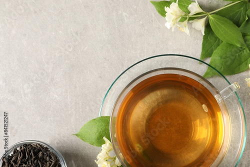 Aromatic jasmine tea in cup, flowers and dry leaves on light grey table, flat lay. Space for text