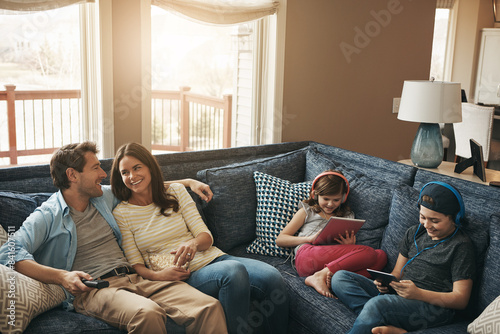 Family, children and parents on couch, watching tv or streaming on tablet with bonding in living room. Mother, father and kids with electronics, popcorn or movies to relax with show on sofa at house