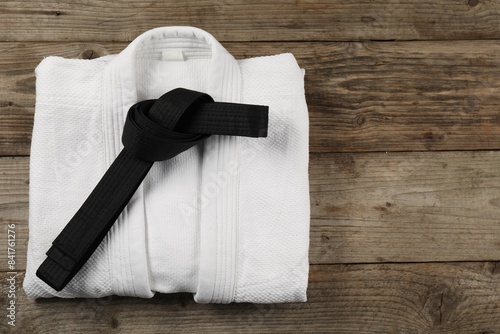 Black karate belt and white kimono on wooden background, top view. Space for text