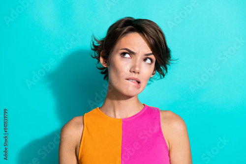 Photo of uncertain unsure woman wear pink orange top biting lip looking empty space isolated teal color background