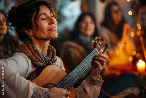 A woman plays acoustic guitar with her eyes closed, enjoying the moment in a cozy and warm setting.