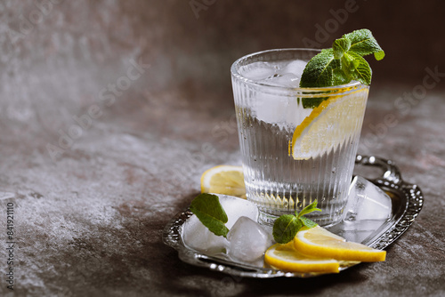 Glass of refreshing sparkling water with ice, lemon and mint on silver tray