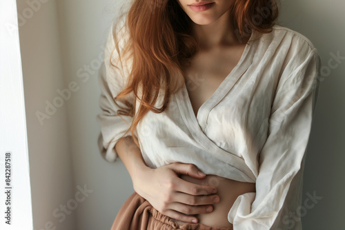 A close-up of a woman holding their stomach with a pained expression, showing abdominal pain