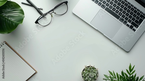 Flat Lay of a White Desk with Laptop, Glasses, Pens, Notebook, and Plants
