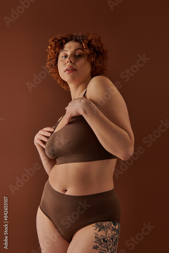Curvy redhead woman elegantly posing in a brown bikini.
