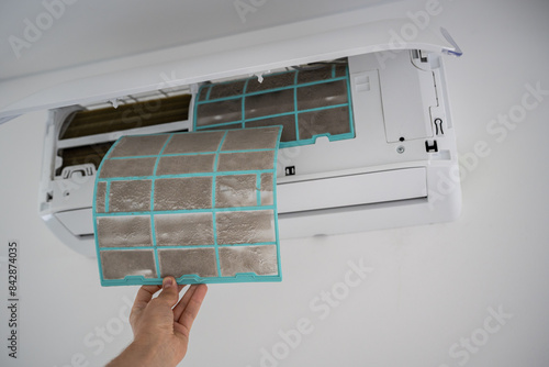 Person removing dirty dusty air conditioner coarse filter for washing, cleaning. Home air conditioner service maintenance, repair and clean equipment. Dust - cause of illness. Closeup.