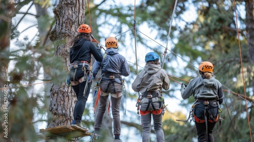 Four workers wearing harnesses and guiding each other on a high ropes course emphasizing teamwork and safety protocols.