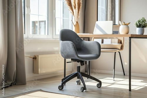 A grey office chair with wheels stands in a modern home office, near a wooden desk and window.