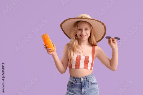 Beautiful girl with bottle of sunscreen spray and sunglasses on lilac background