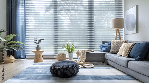 Window blinds in modern living room with blue and white stripes, large windows with sheer shades and sofa.