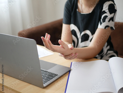 A young Asian woman working at the office feels pain in her wrists from typing from a laptop for a long time. Pain and numbness in the wrist Health care and medical concept