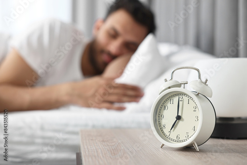 Man sleeping on bed at morning, focus on alarm clock