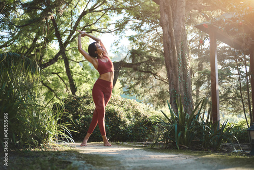 Fit sporty happy young Hispanic woman wearing sportswear meditating doing yoga breathing stretching exercises standing in nature park outdoors in sunny morning. Authentic candid photo.