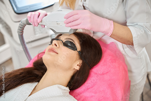 Young woman undergoing intense pulsed light therapy done by beautician