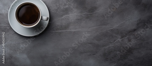 The image features a bird s eye view of a black cup filled with coffee on a gray table The background is devoid of any distractions. Copyspace image