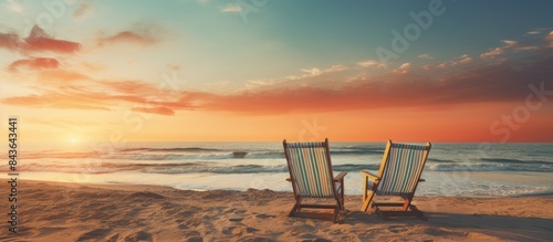 A picturesque sunset beach scene with vintage aesthetics showcasing beach chairs on the sandy shore creating a tranquil summer background perfect for a copy space image
