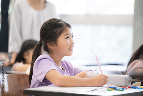 教室で授業中に勉強をし鉛筆を持つ小学生の女の子見上げて黒板を写す