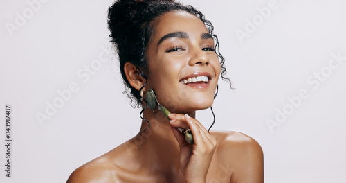 Face roller, beauty and woman with cosmetics, dermatology and grooming routine on grey studio background. Portrait, person and model with tool, wellness and smile with skincare, treatment and glow