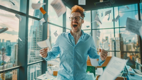 An excited businessman celebrating with arms raised, surrounded by flying papers in a modern office with a city skyline. Achievement and victory concept.