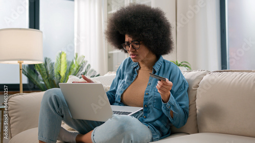 Confused puzzled irritated upset girl buyer African American woman try pay online with laptop credit card failure error mistake secure number shopping problem unsuccessful payment bank trouble at home