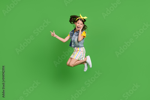 Photo of positive amazed kid girl jump point empty space isolated green color background