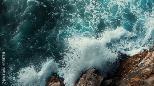 An aerial shot captures the raw power and beauty of waves crashing against rocky cliffs